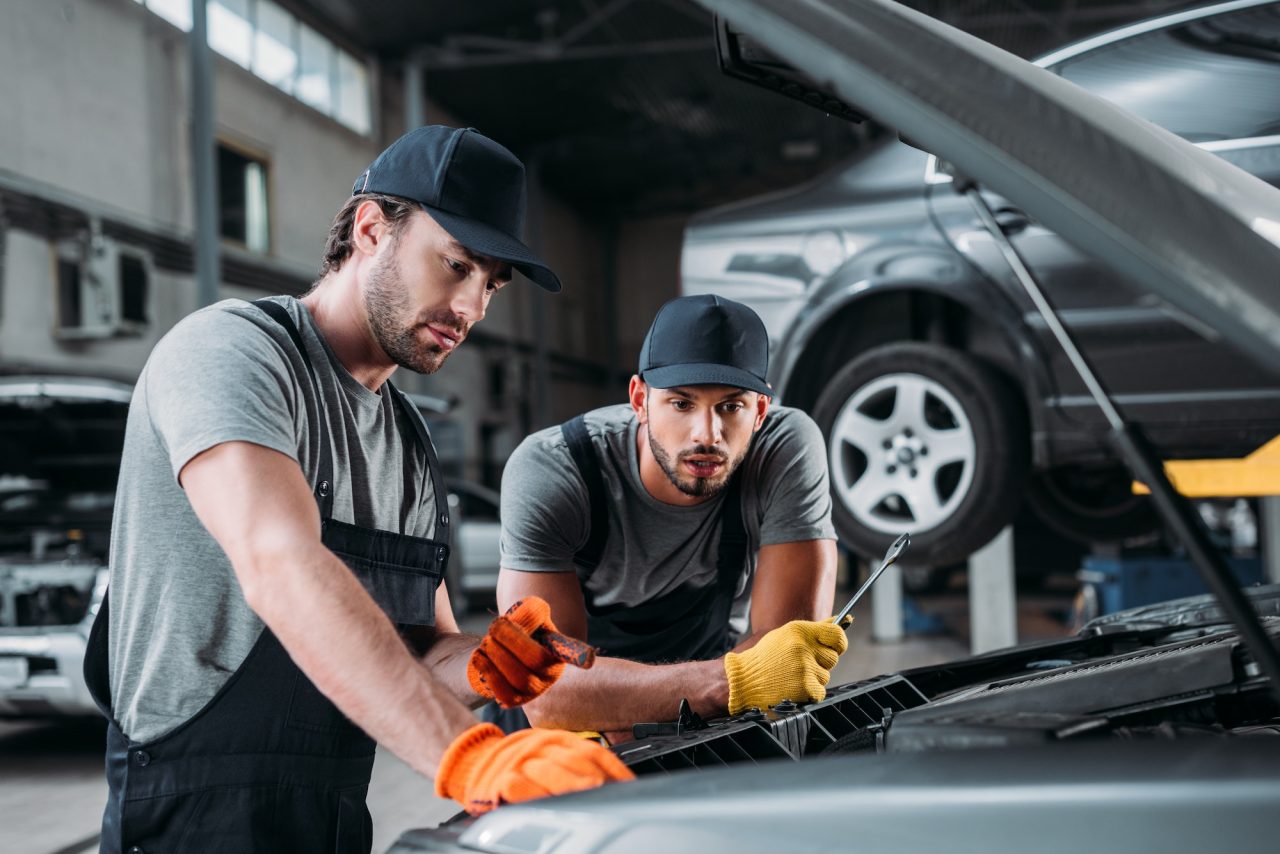 two auto mechanics inspecting under a car hood