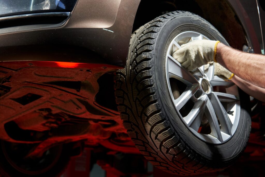 The hands of an auto mechanic take off, dismantle, hang up a car wheel holding the spokes of an alloy wheel. the car is raised on a lift, you can see the bottom