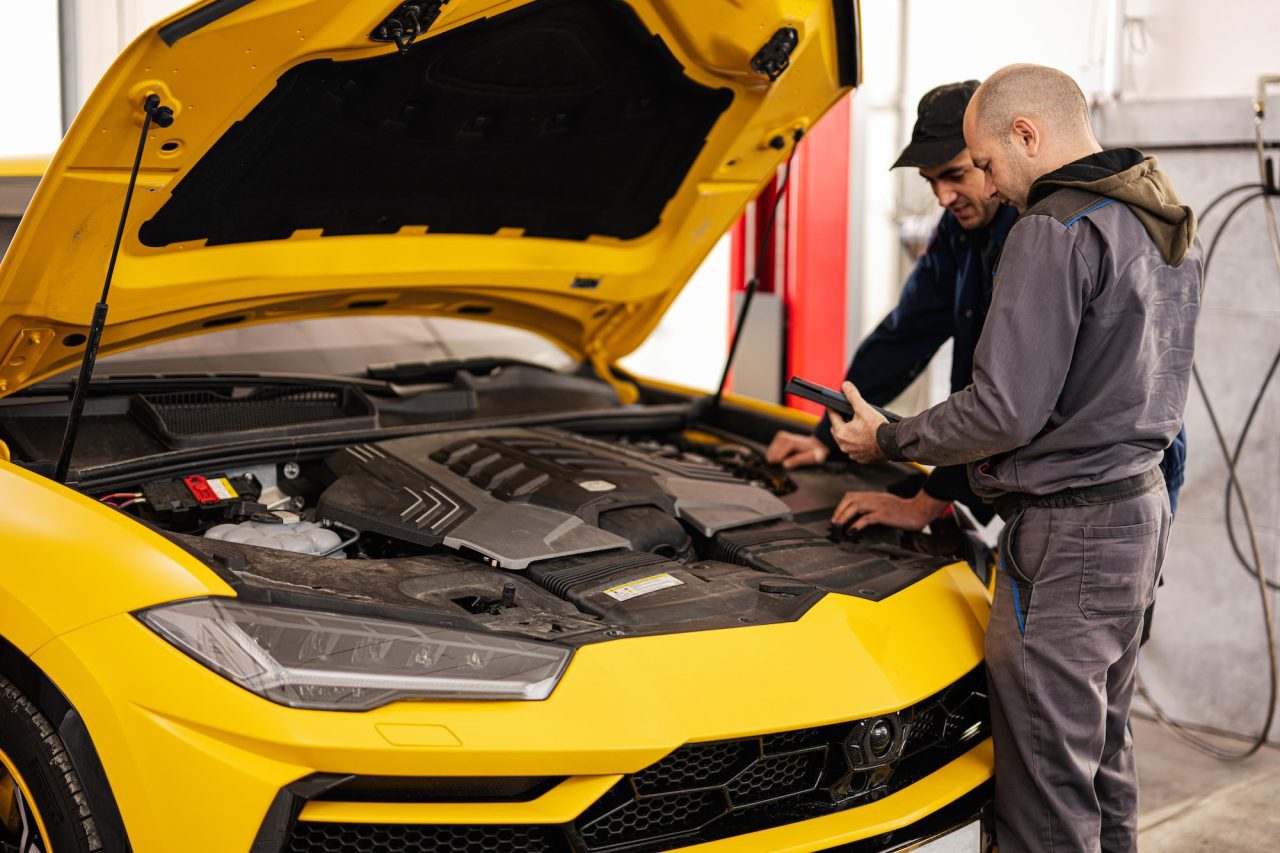 two auto mechanics inspecting a car under the hood