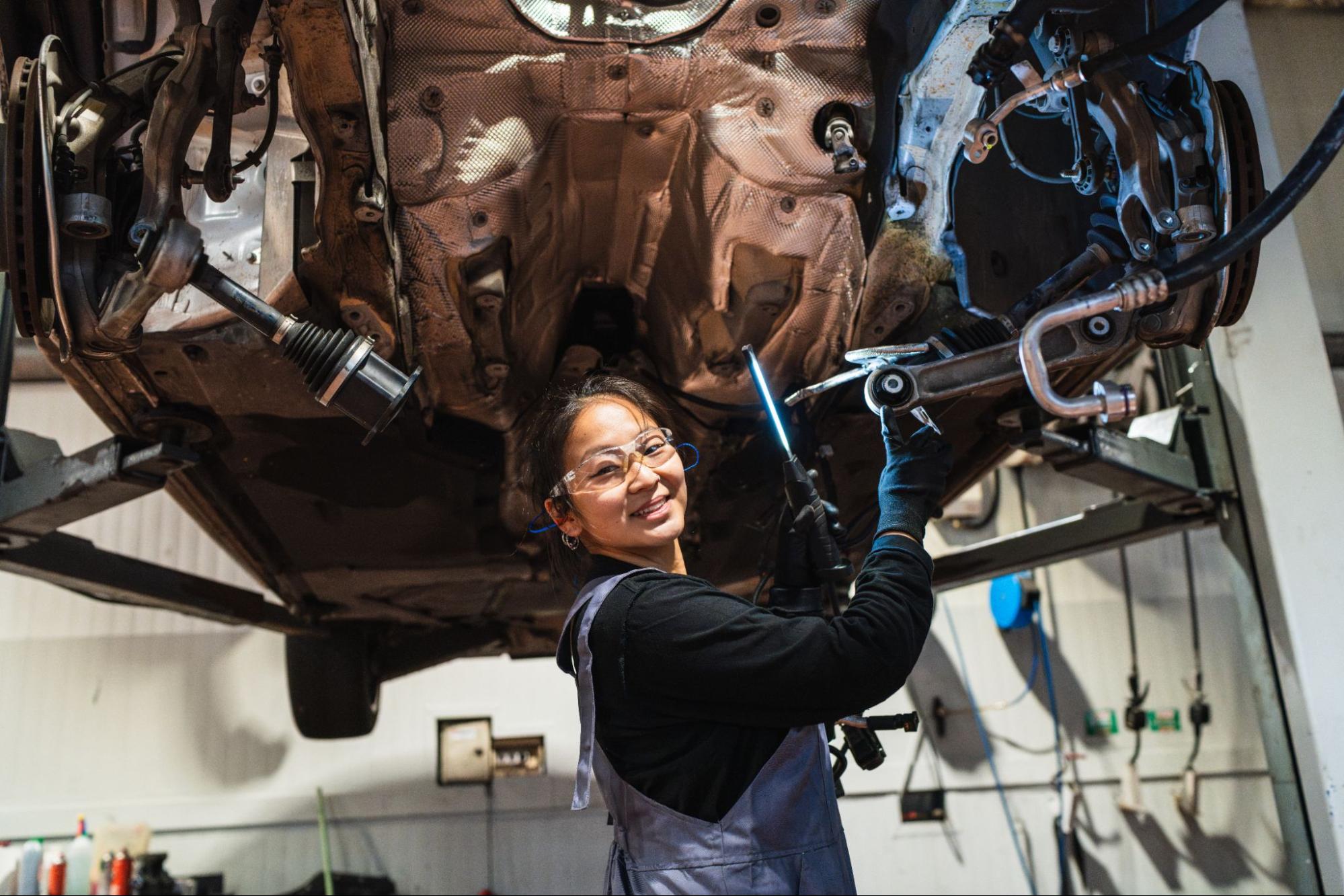 An Asian female mechanic repairs a car chassis in the shop.
