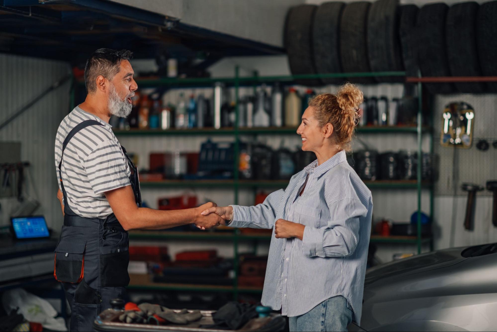 A satisfied female customer shakes hands with the auto shop mechanic