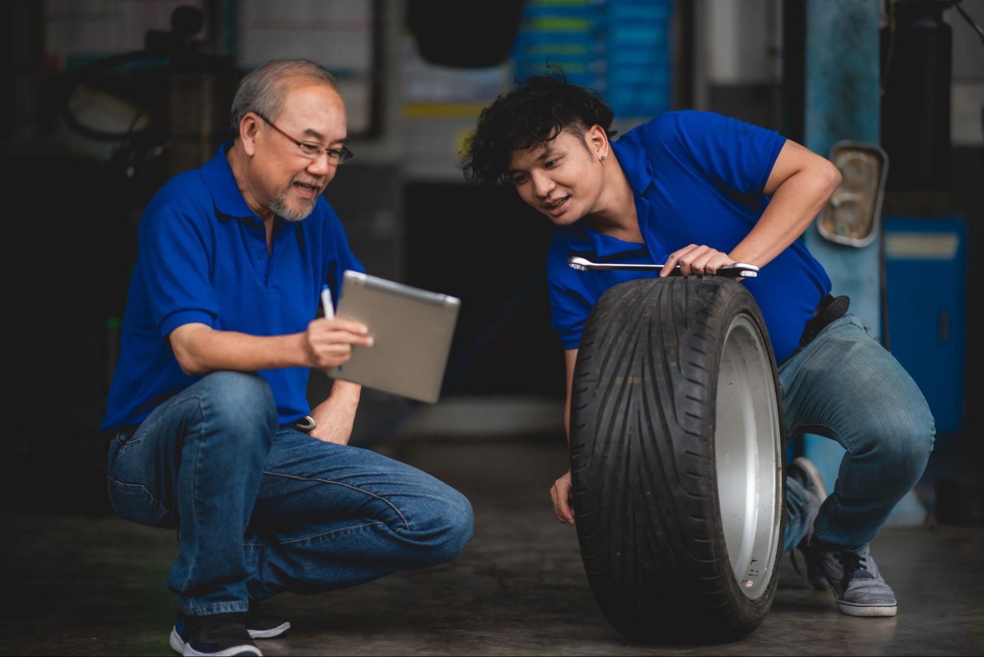 Two mechanics in a repair garage inspecting a tire.