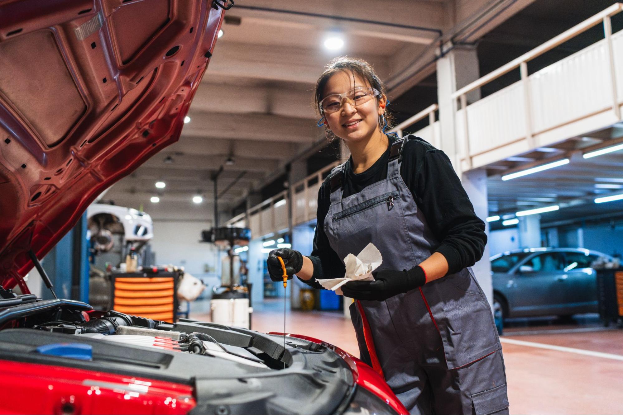 A female Chinese mechanic checks a car’s oil level in an auto repair shop.