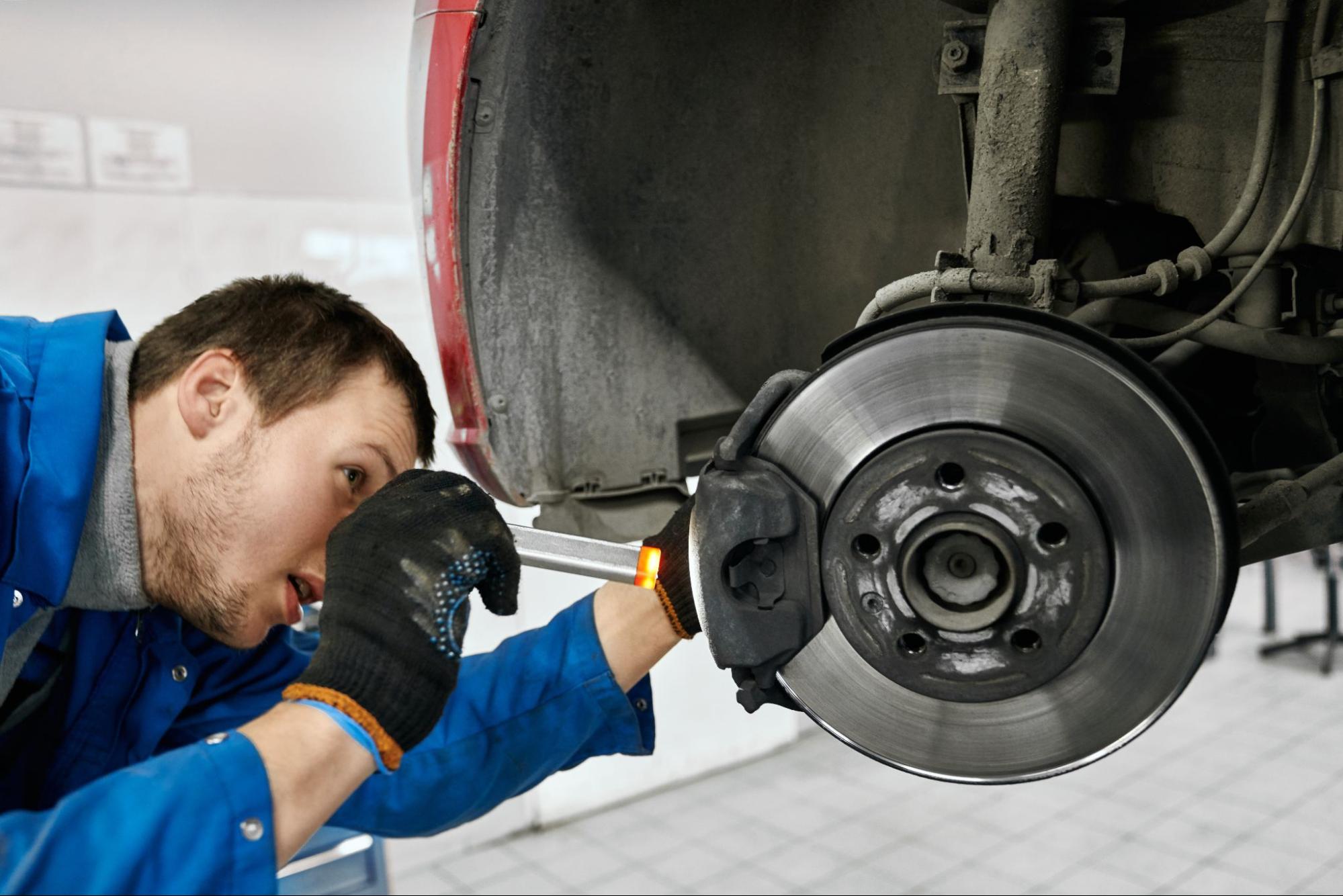 Close-up of a male mechanic using a flashlight to inspect brake pads.